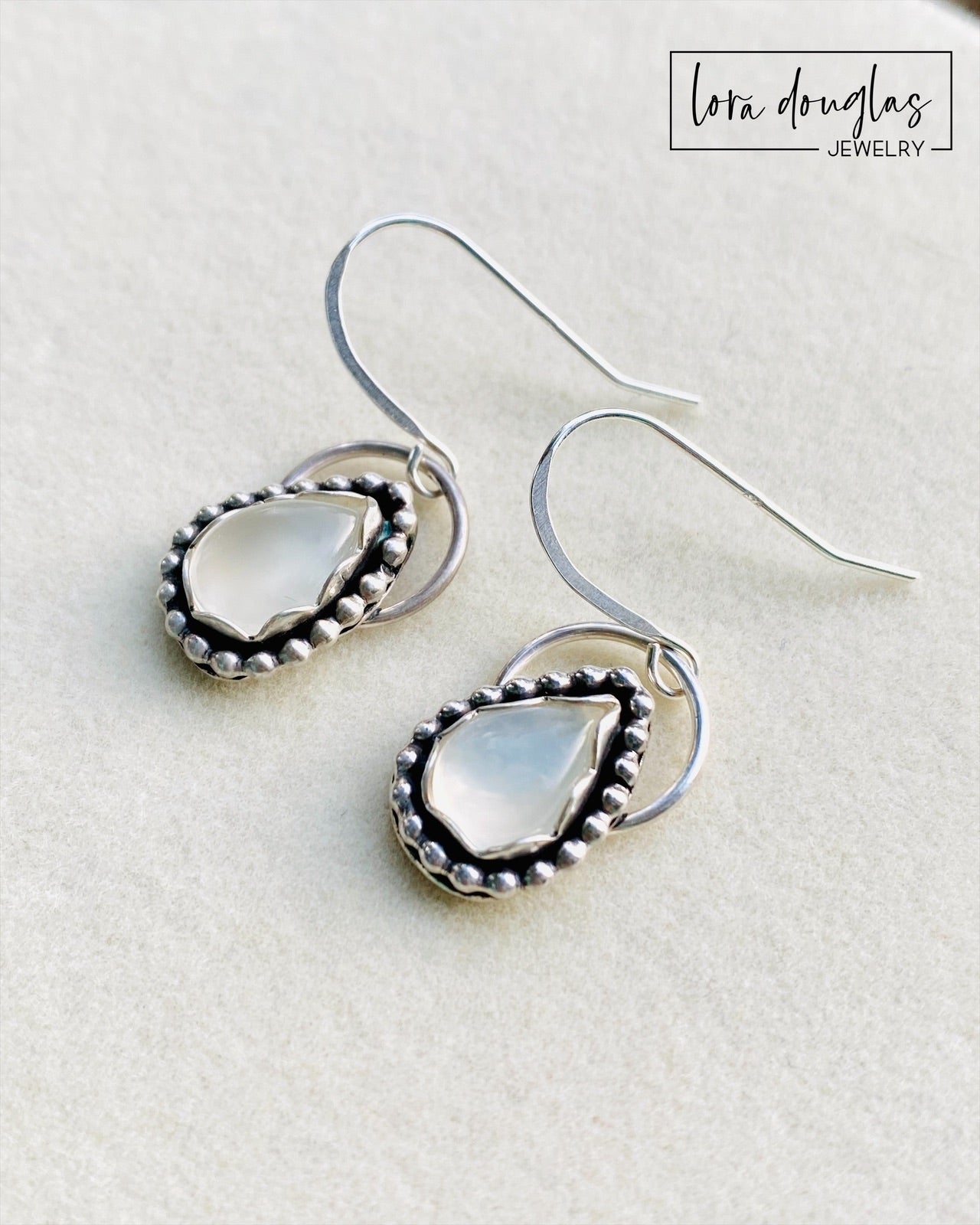 A pair of sterling silver dangle earrings with a teardrop-shaped moonstone stone in the center