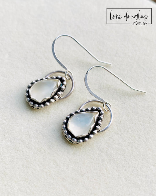 A pair of sterling silver dangle earrings with a teardrop-shaped moonstone stone in the center