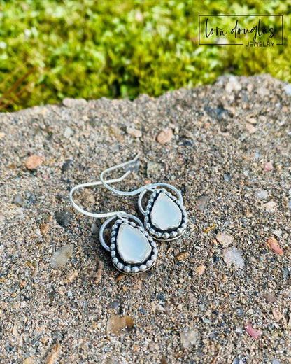 A pair of sterling silver dangle earrings with a teardrop-shaped moonstone stone in the center