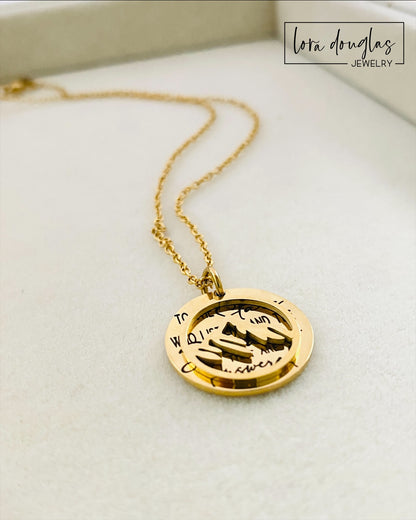 A gold stainless steel necklace with a round pendant engraved with the quote 'To the Stars who listen - and the Dreams that are Answered' and a laser cut mountain pendant.
