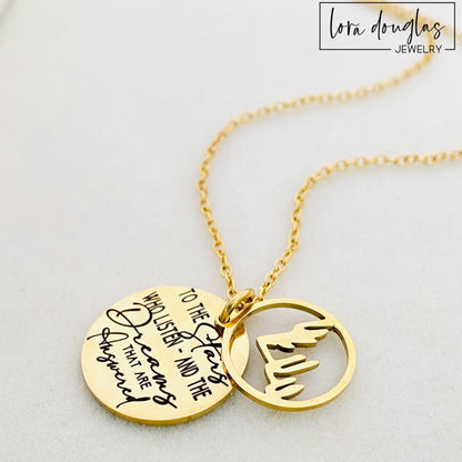 A gold stainless steel necklace with a round pendant engraved with the quote 'To the Stars who listen - and the Dreams that are Answered' and a laser cut mountain pendant.