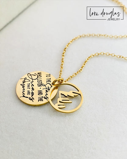 A gold stainless steel necklace with a round pendant engraved with the quote 'To the Stars who listen - and the Dreams that are Answered' and a laser cut mountain pendant.