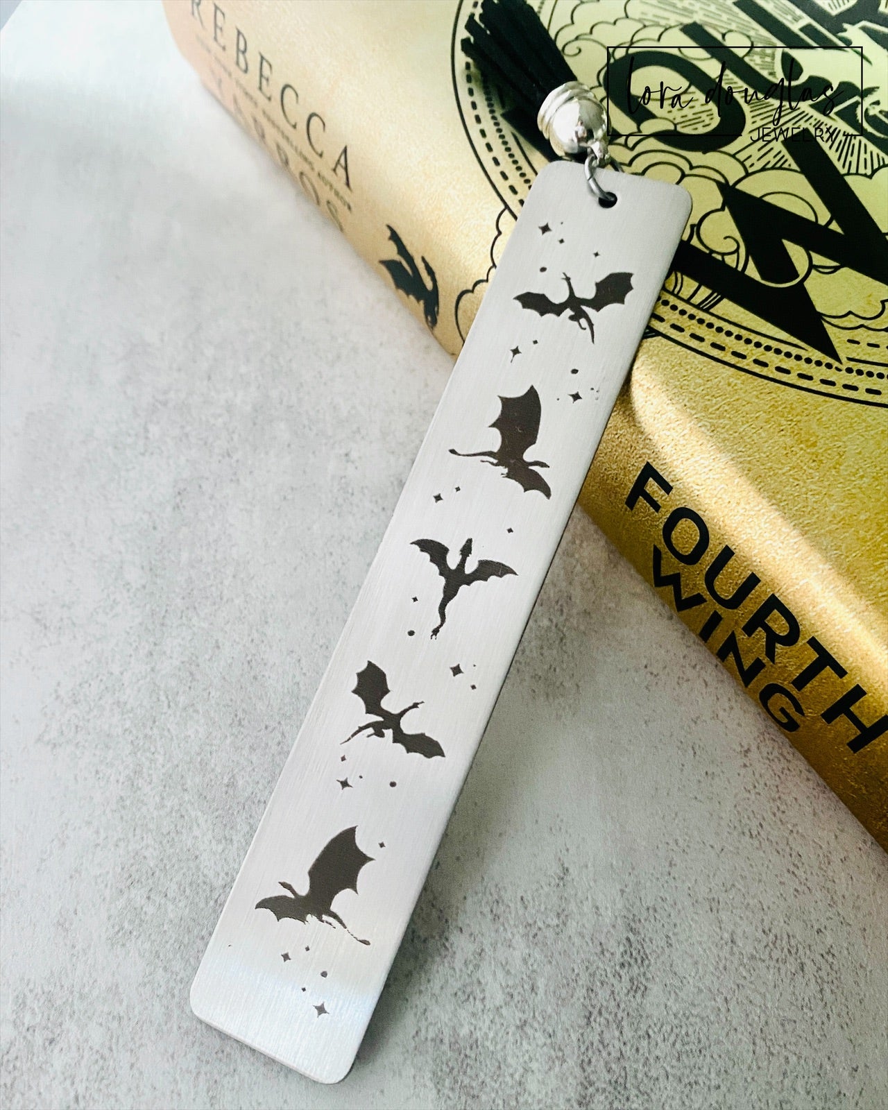 Silver stainless steel bookmark with engraved dragons sitting beside a copy of Fourth Wing Novel