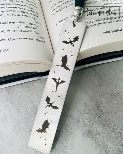 Silver stainless steel bookmark with engraved dragons sitting beside a copy of Fourth Wing Novel