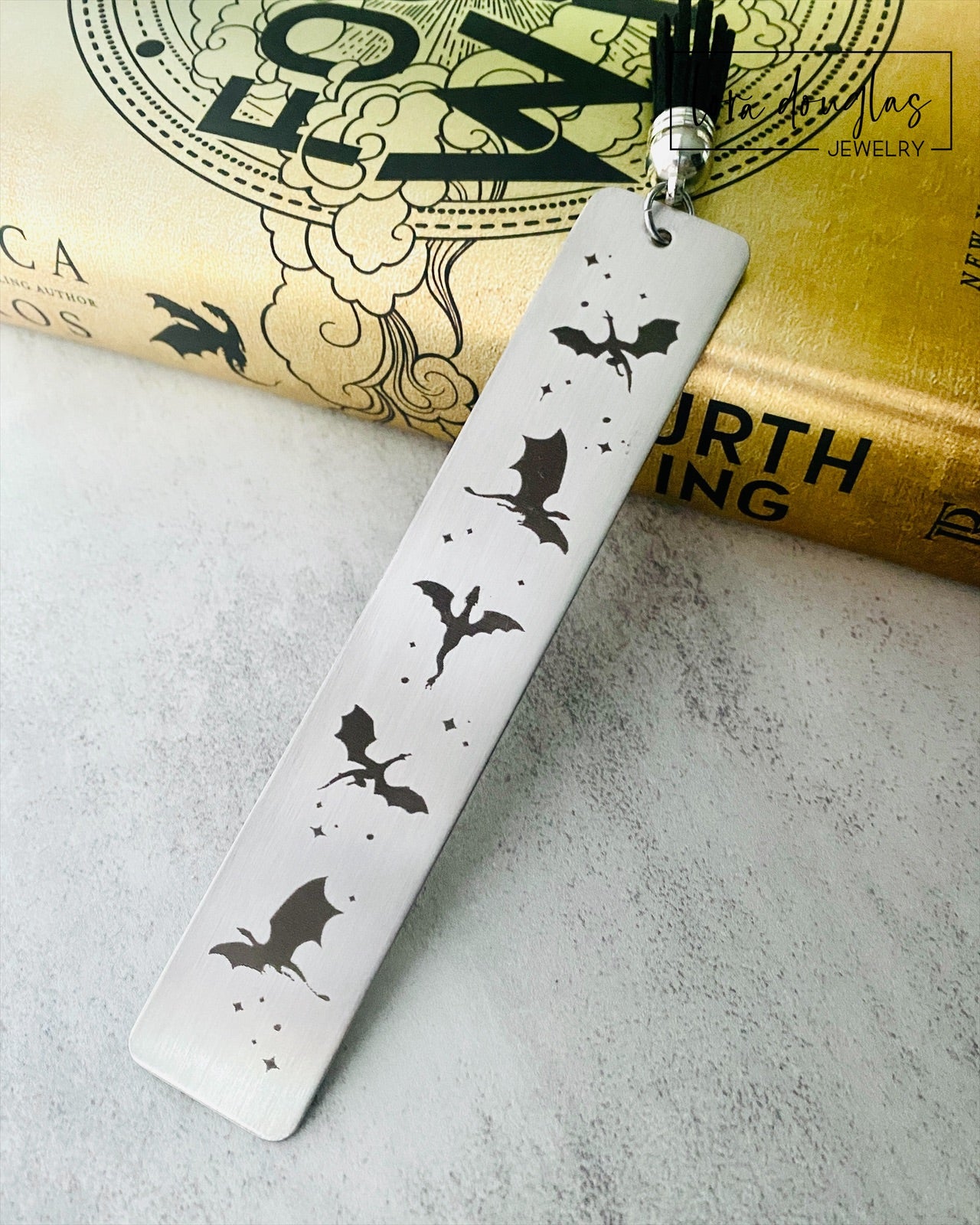 Silver stainless steel bookmark with engraved dragons sitting beside a copy of Fourth Wing Novel