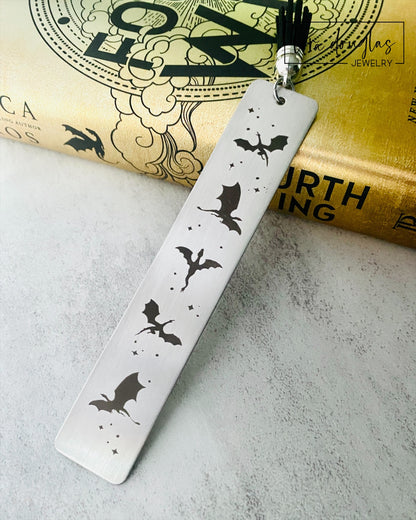Silver stainless steel bookmark with engraved dragons sitting beside a copy of Fourth Wing Novel
