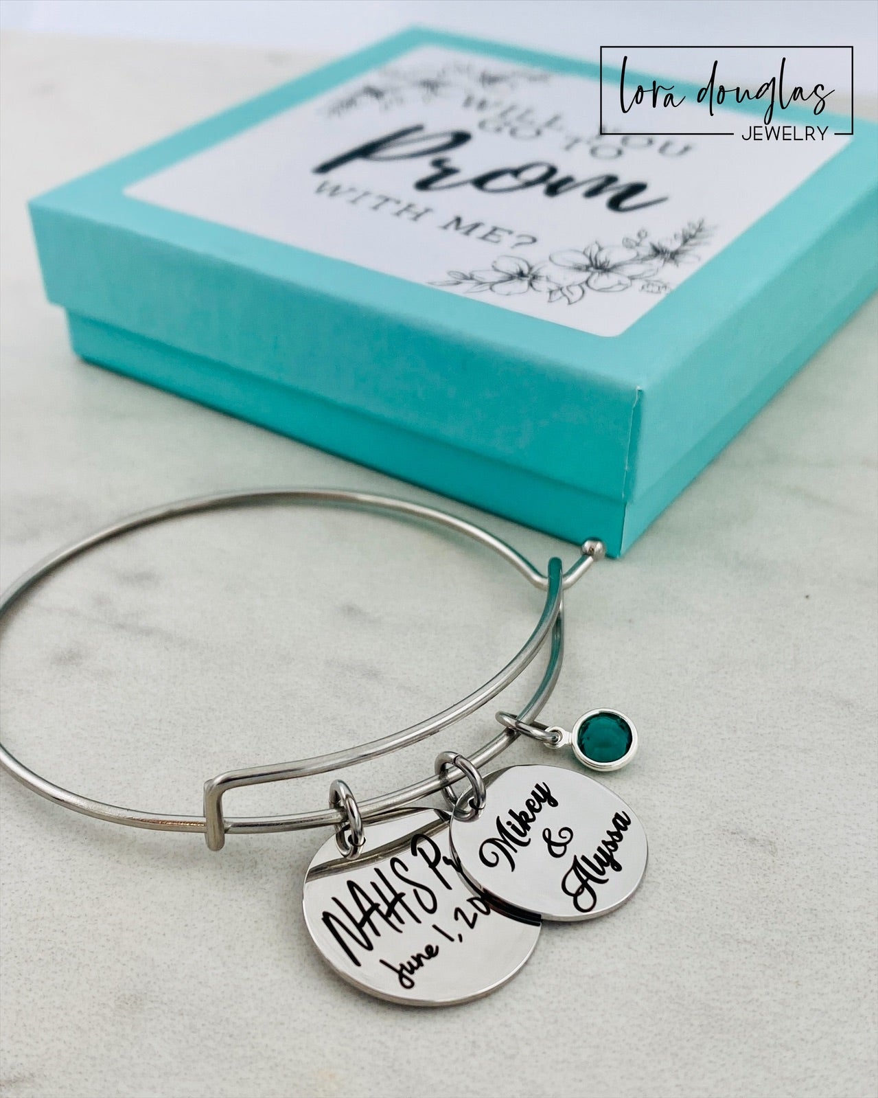 A stainless steel bangle bracelet with personalized engravings, presented in a blue box with 'Promposal' text.