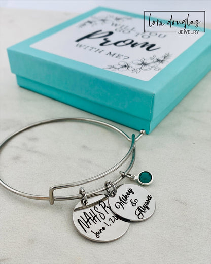 A stainless steel bangle bracelet with personalized engravings, presented in a blue box with 'Promposal' text.