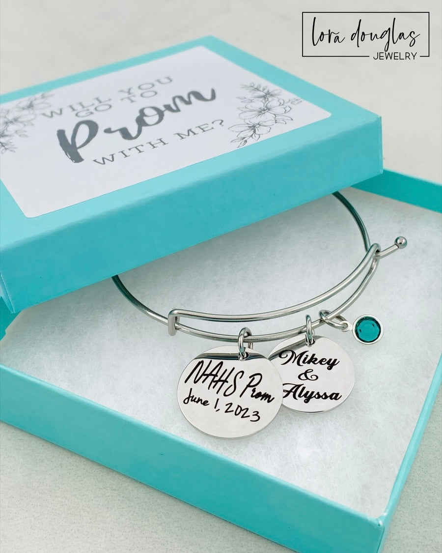 A stainless steel bangle bracelet with personalized engravings, presented in a blue box with 'Promposal' text.