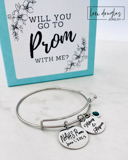 A stainless steel bangle bracelet with personalized engravings, presented in a blue box with 'Promposal' text.