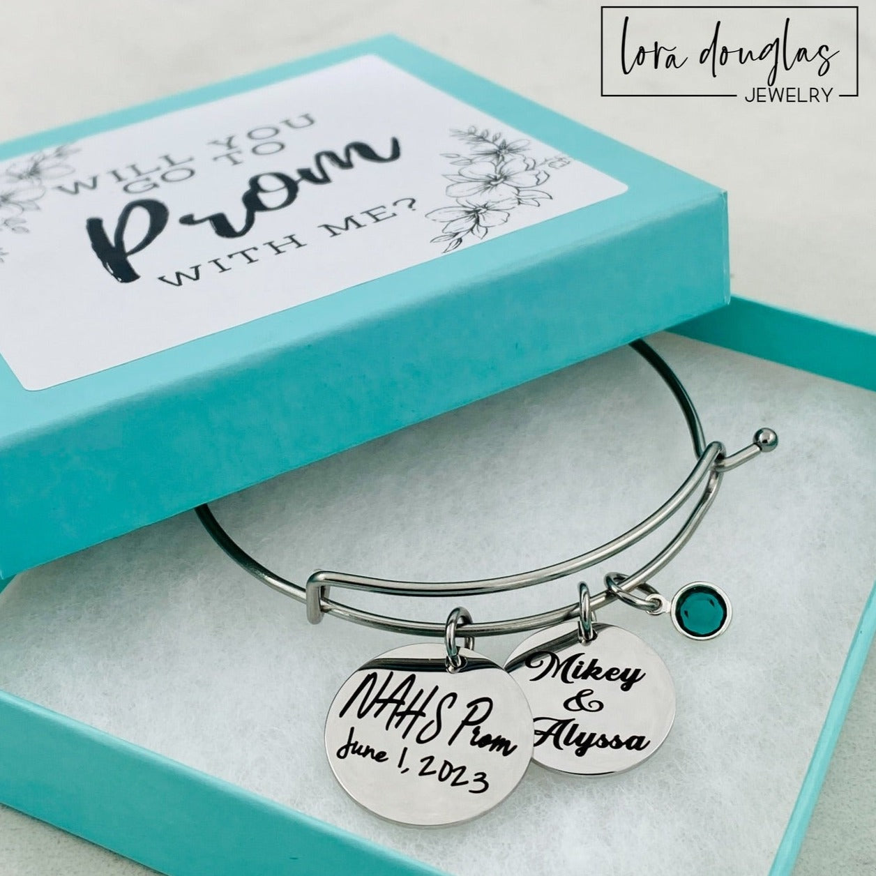 A stainless steel bangle bracelet with personalized engravings, presented in a blue box with 'Promposal' text.