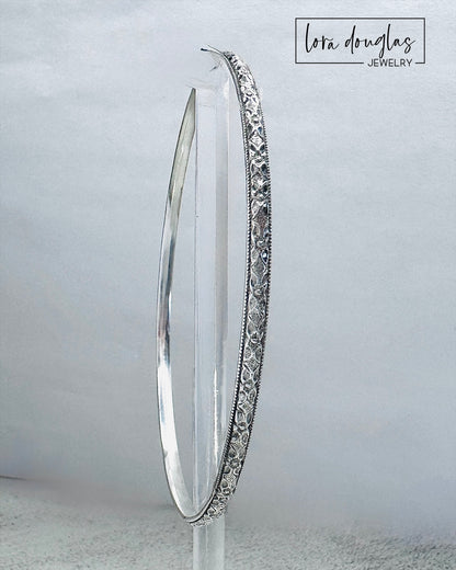 Handcrafted sterling silver bangle bracelet with textured and polished finish displayed on clear stand.