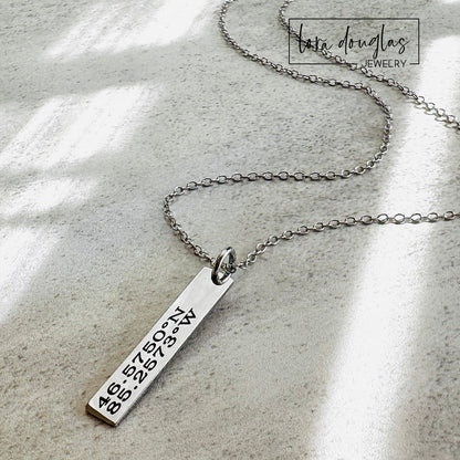 A custom necklace engraved with GPS coordinates or latitude and longitude of a special place on a silver stainless steel pendant and chain