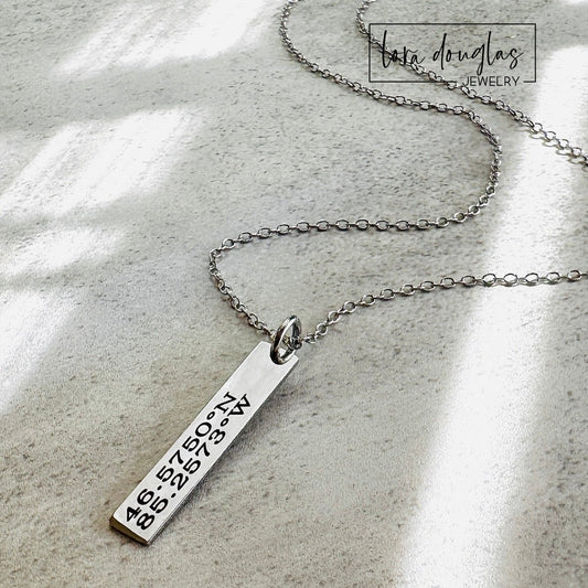 A custom necklace engraved with GPS coordinates or latitude and longitude of a special place on a silver stainless steel pendant and chain