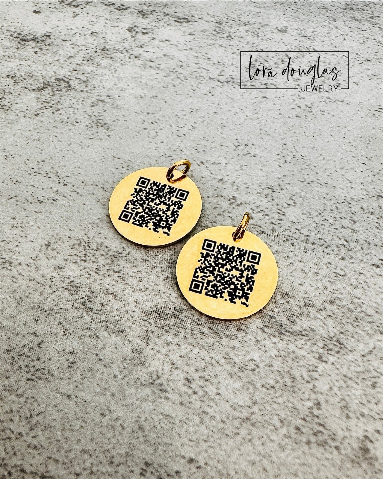 Two gold round pendants with QR codes on a gray textured surface