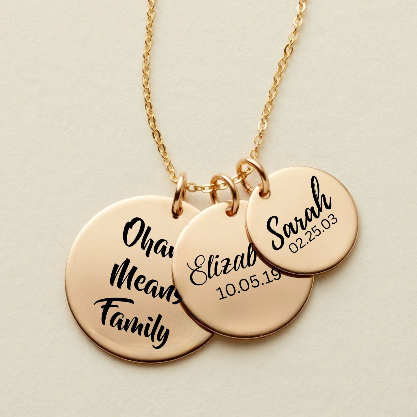 rose Gold necklace with three round pendants engraved with names and dates on a beige background