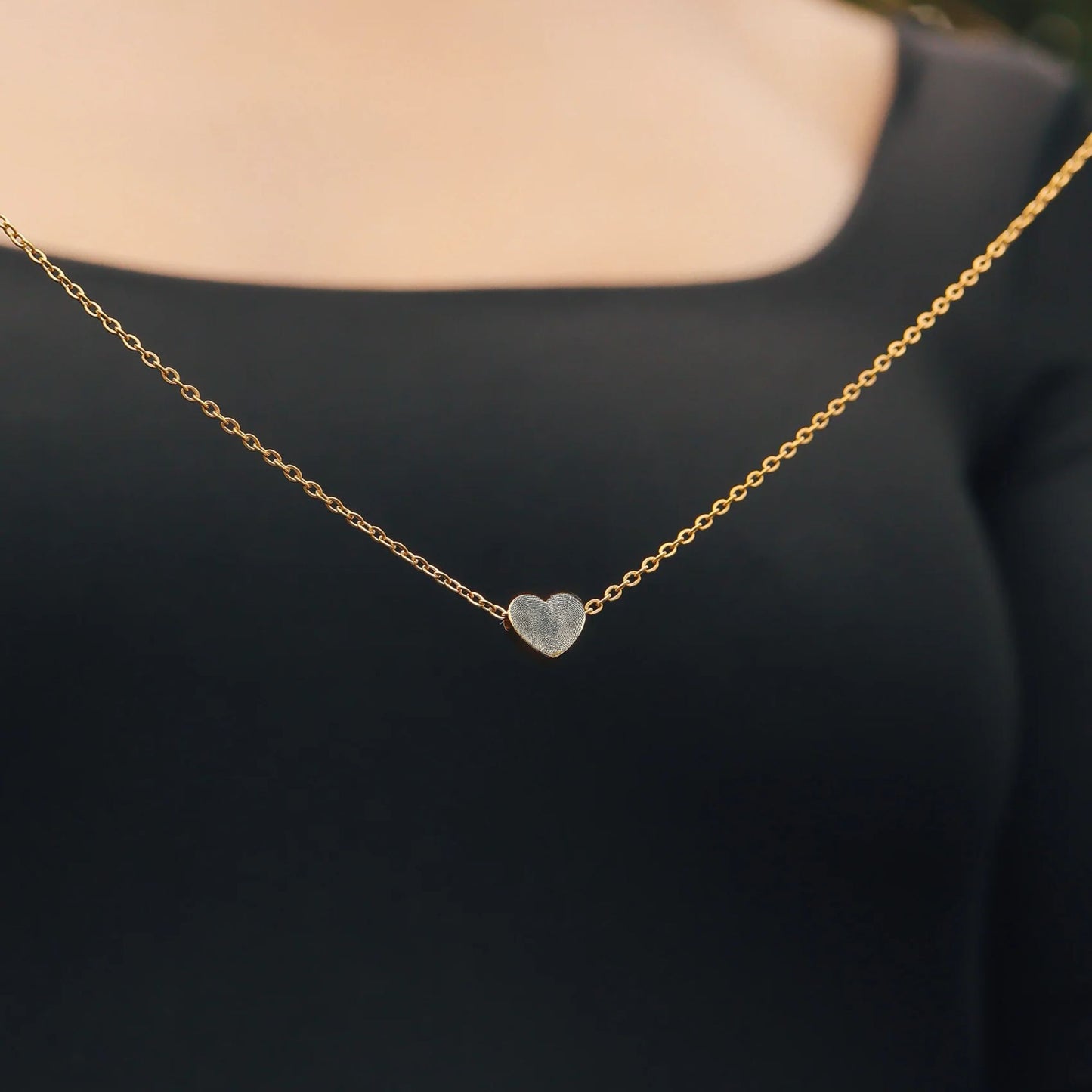 Gold necklace with a heart-shaped pendant engraved with a fingerprint on a black background