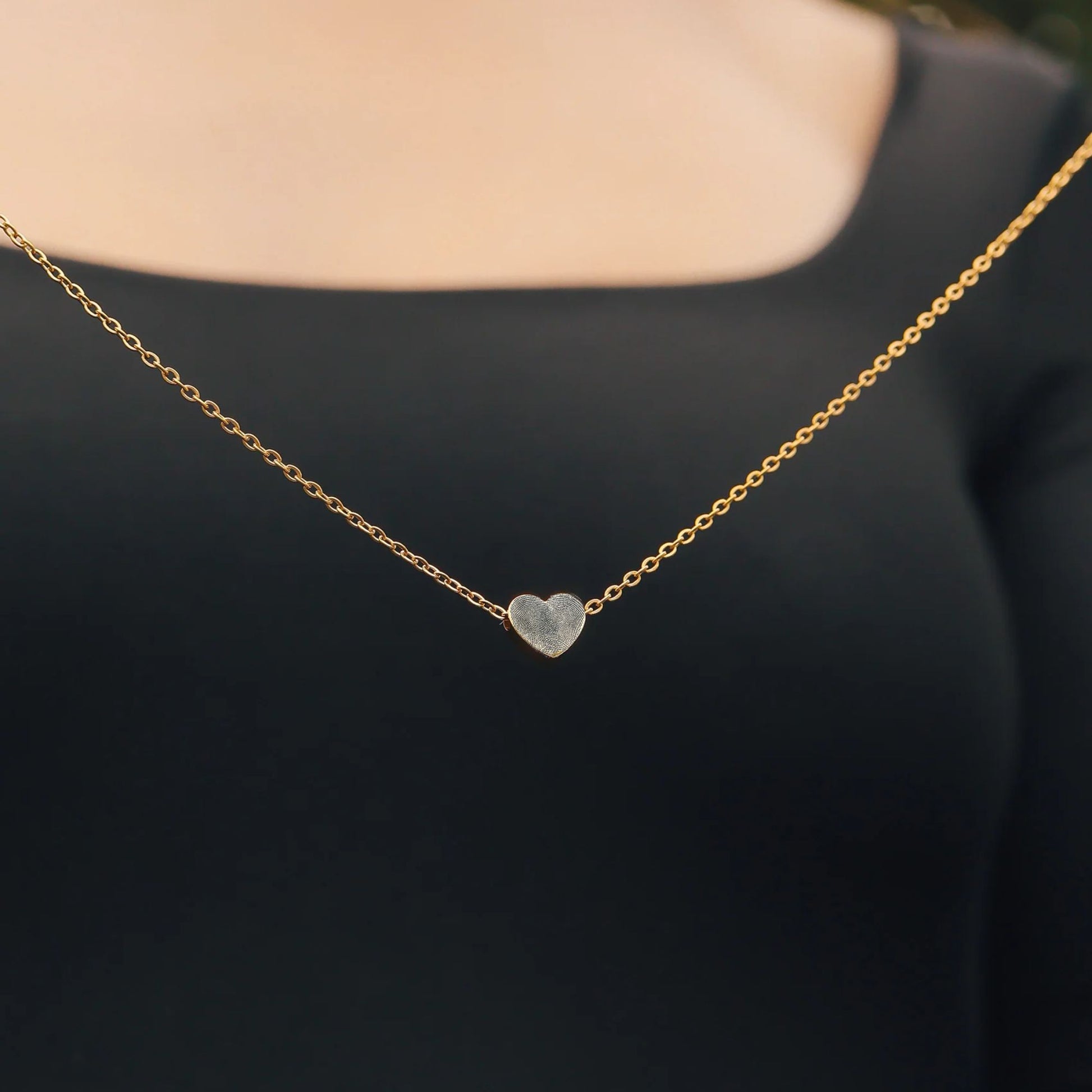 Gold necklace with a heart-shaped pendant engraved with a fingerprint on a black background