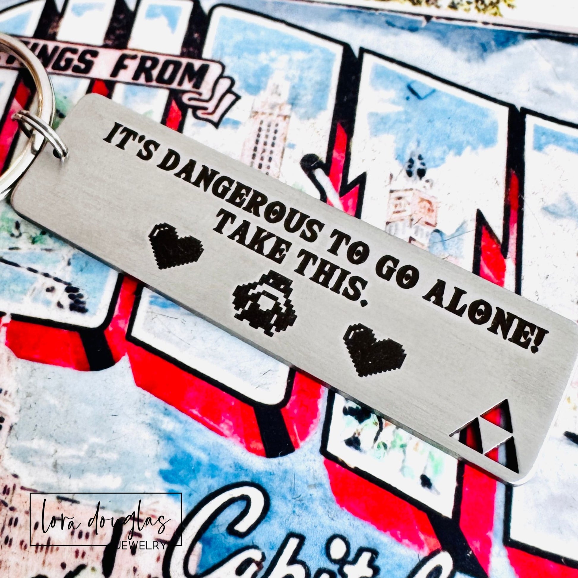 Metal keychain with text 'It's dangerous to go alone! Take this.' on a colorful background.