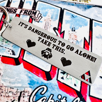 Metal keychain with text 'It's dangerous to go alone! Take this.' on a colorful background.