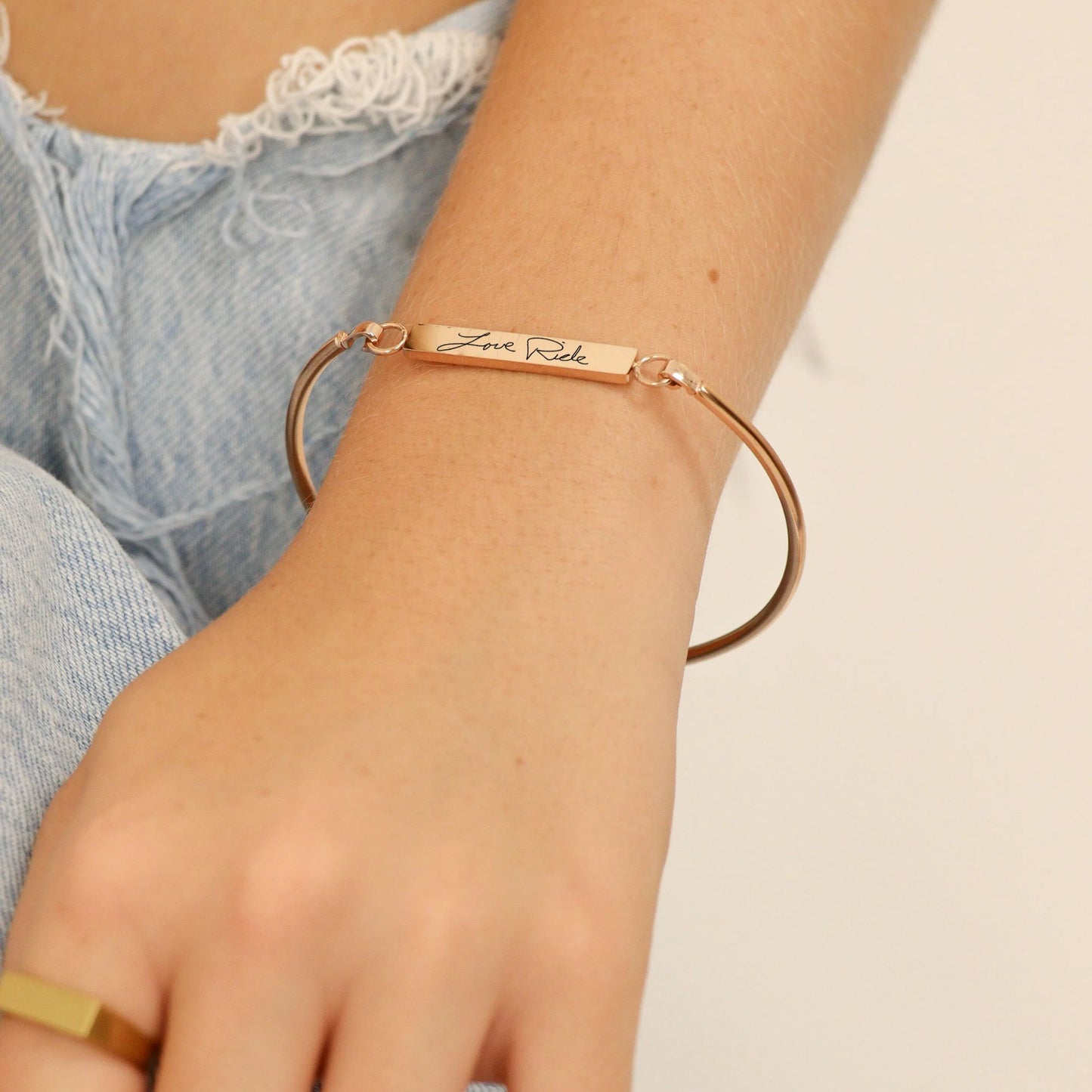 gold bracelet with engraved text on a wrist against a neutral background