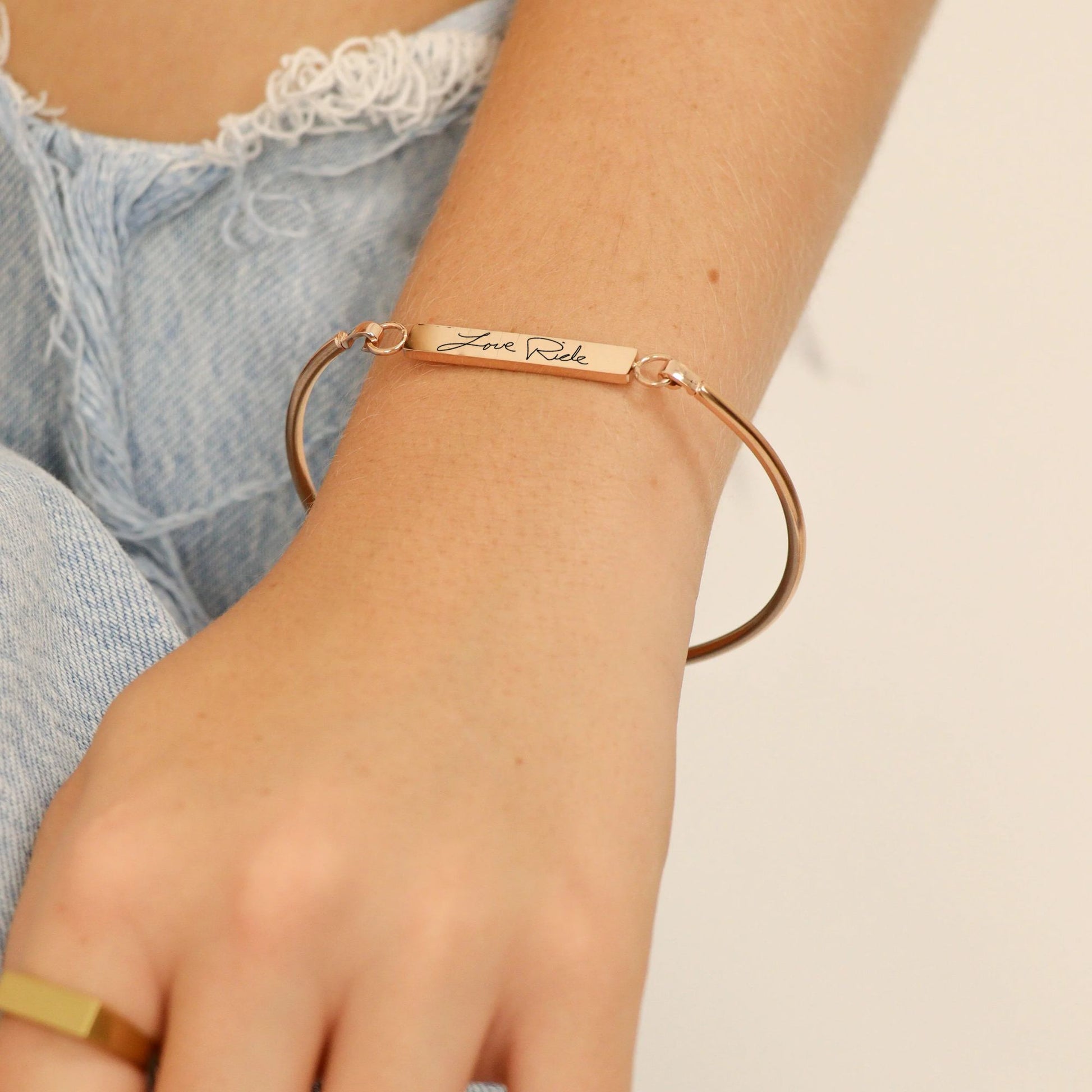gold bracelet with engraved text on a wrist against a neutral background