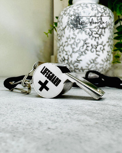 whistle with 'Lifeguard' and cross symbol engraved on a textured surface with blurred background
