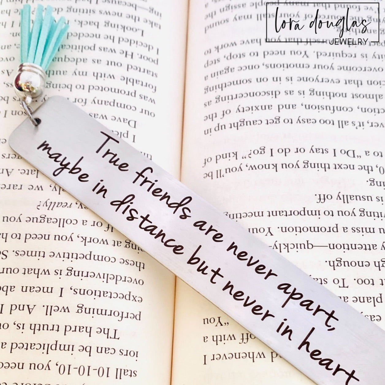 long distance friendship bookmark engraved with True Friends Are Never Apart quote on stainless steel metal bookmark with leather tassel, personalized friendship gift displayed inside open book with brushed silver finish