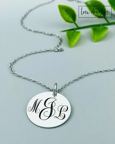 Silver necklace with a round pendant featuring initials on a light gray background.