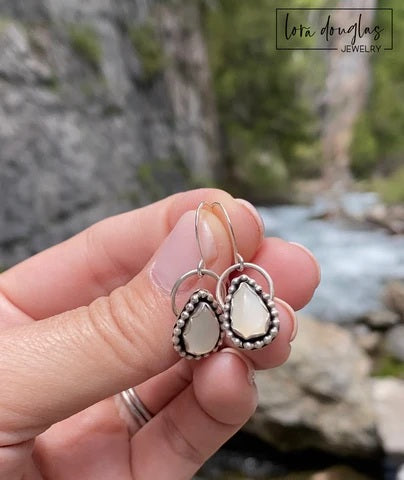 A pair of sterling silver dangle earrings with a teardrop-shaped moonstone stone in the center