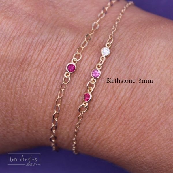Gold bracelet with pink and red gemstones on a wrist, branded 'lora Douglas Jewelry'.
