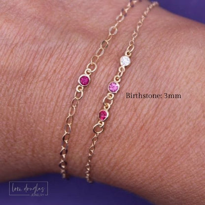 Gold bracelet with pink and red gemstones on a wrist, branded 'lora Douglas Jewelry'.