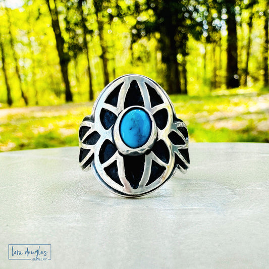 Sterling silver ring with blue stone on a white surface with a blurred green forest background
