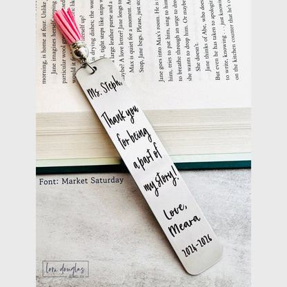 personalized metal bookmark with permanent laser engraving and tassel shown inside an open novel, stainless steel reader gift perfect for teacher appreciation, graduation celebrations, and encouragement gifts