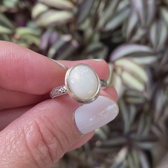 A sterling silver ring with a hand-cut opal cabochon centerpiece, set in an oval setting.