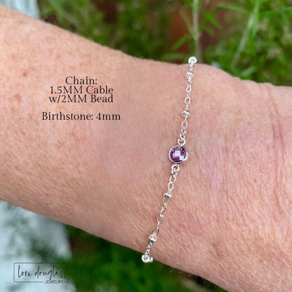 Silver bracelet with a pink bead on a wrist, set against a natural background.