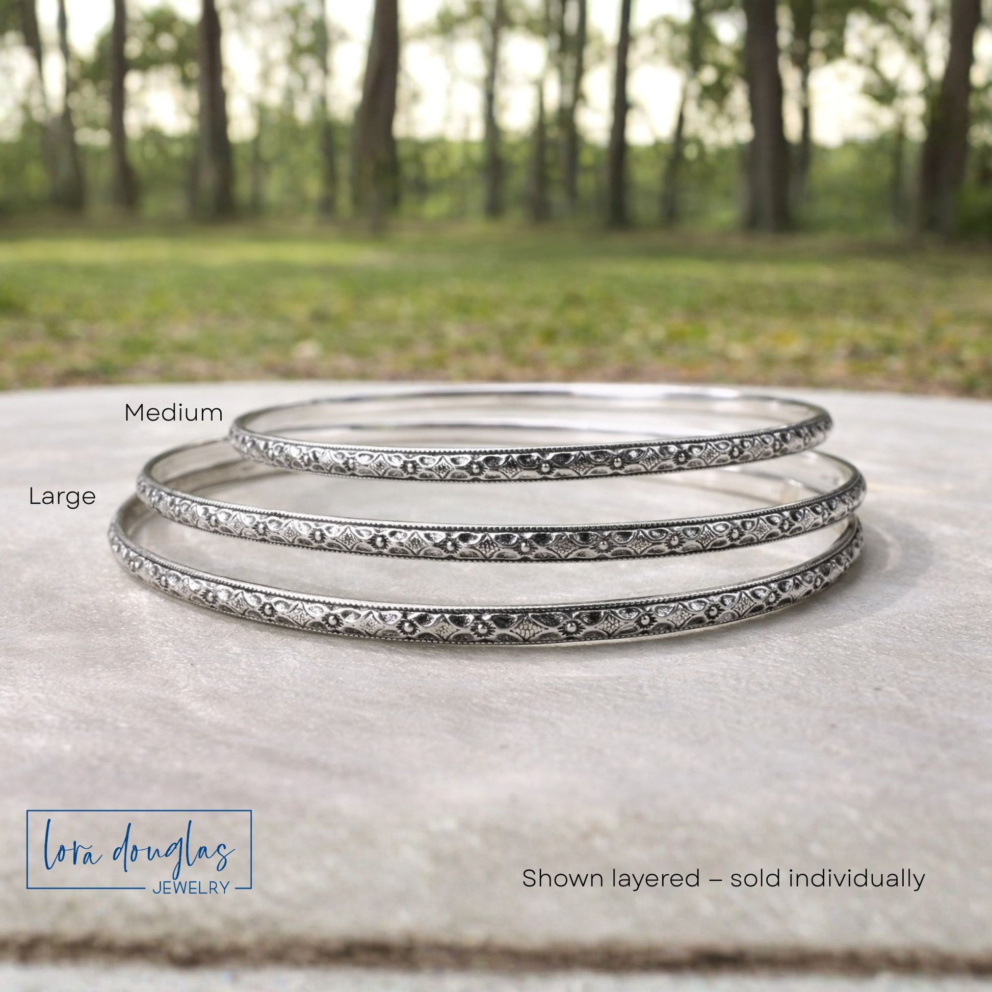 Set of sterling silver bangles with 'Lora Douglas Jewelry' branding on a natural background.