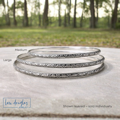 Set of sterling silver bangles with 'Lora Douglas Jewelry' branding on a natural background.