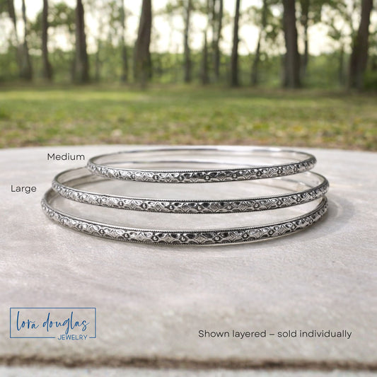 Set of sterling silver bangles with 'Lora Douglas Jewelry' branding on a natural background.