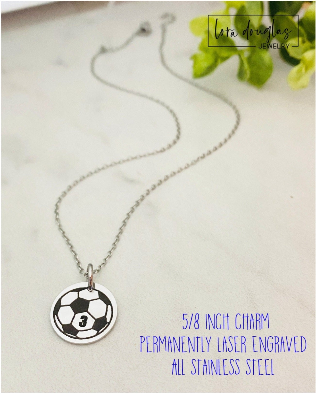 Necklace with soccer ball charm on a light surface with greenery in the background
