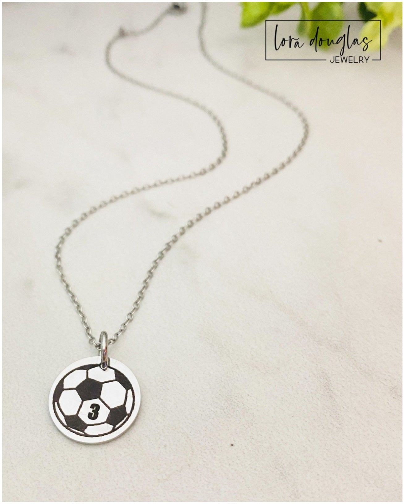 Necklace with a soccer ball pendant personalized with a jersey number on a light gray background