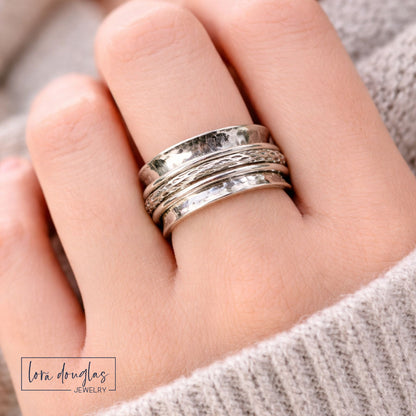 sterling silver spinner ring on hand with wide hammered band and multiple spinning textured rings worn on finger