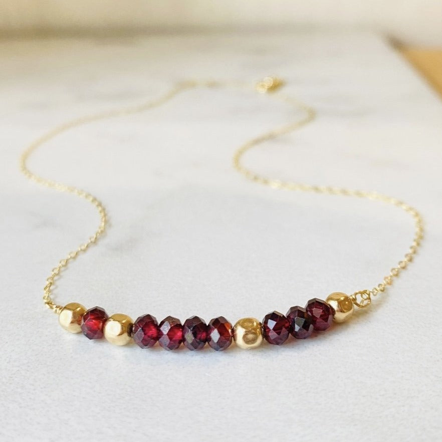 Close view of a 143 necklace showing faceted garnet and gold filled beads used to represent the hidden I Love You message, a subtle piece of romantic jewelry for an anniversary, Valentine's Day or partner gift.
