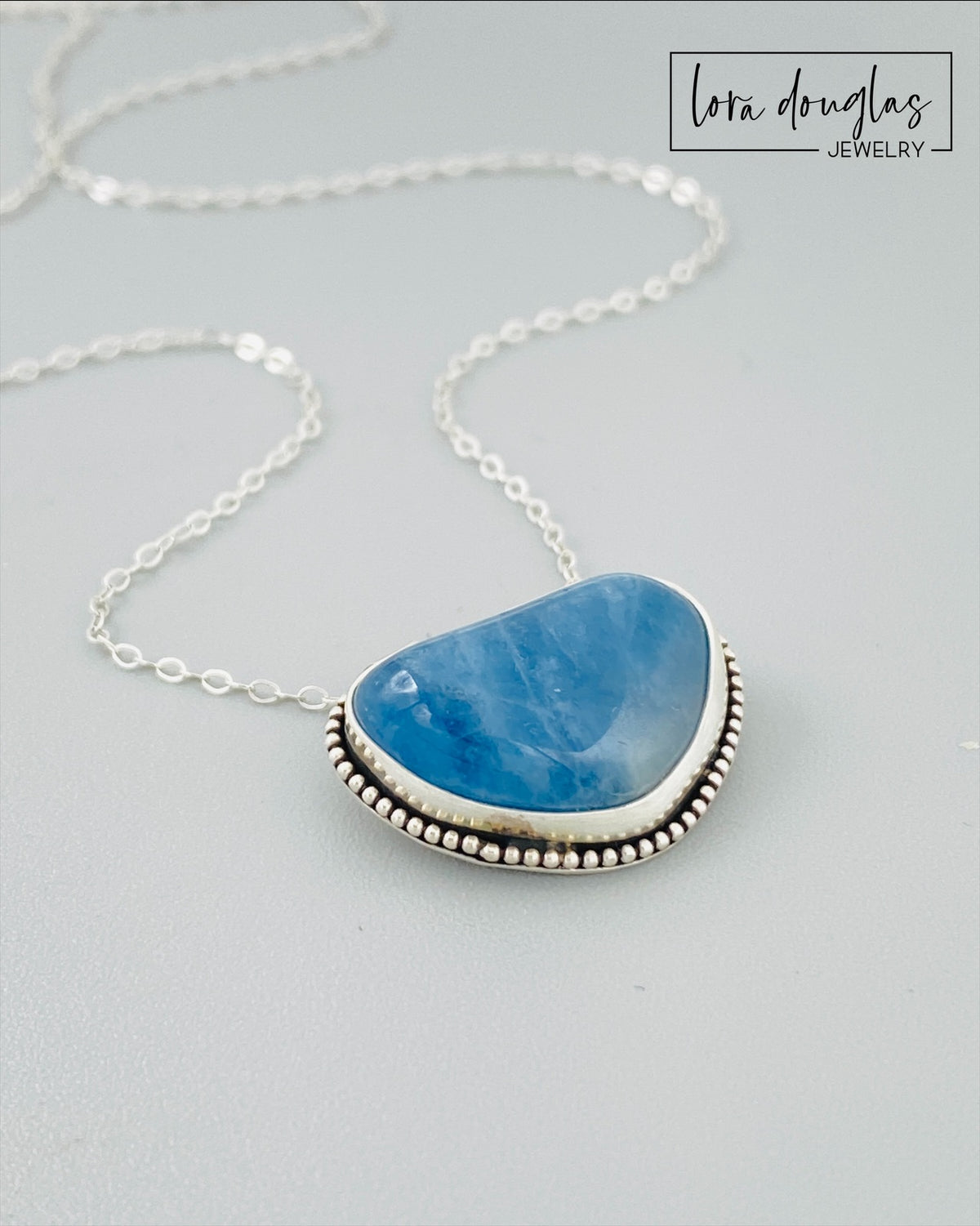 Close view of a natural aquamarine pendant showing the soft ocean blue gemstone and sterling silver setting, paired with an antique patina silver chain for a meaningful March birthstone necklace.
