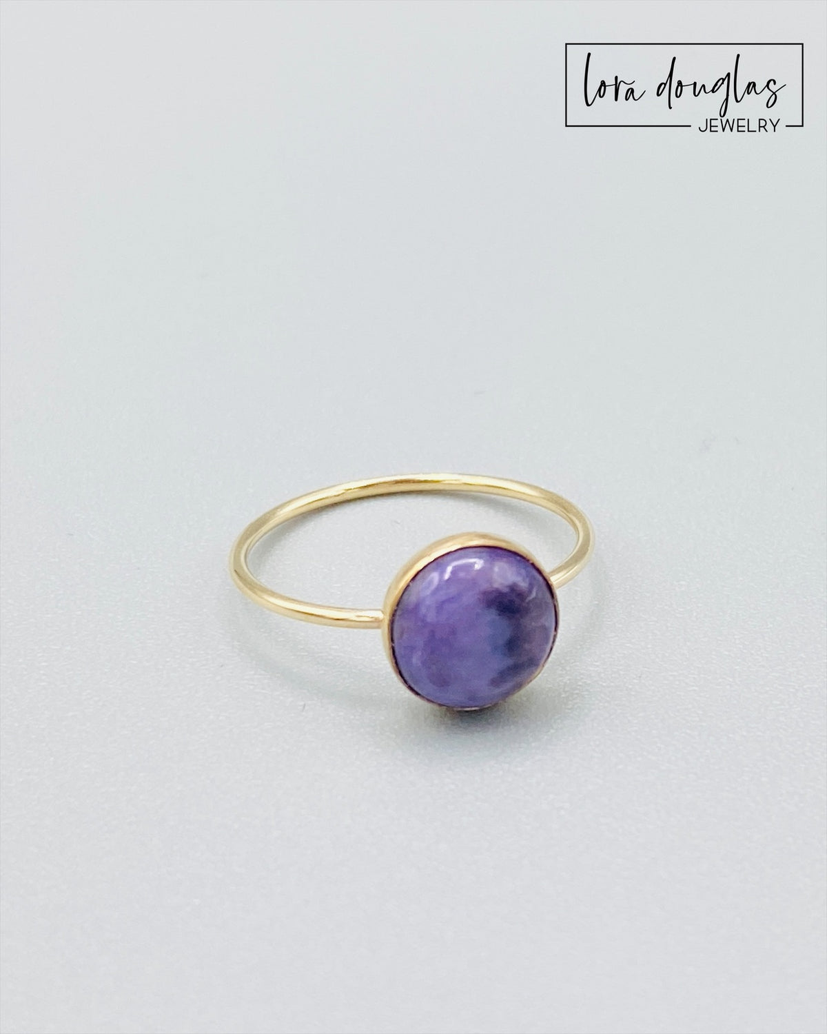 Close view of a natural charoite ring showing the distinctive purple color and individual character of the 8mm gemstone in a warm 14/20 gold filled setting, finished in US ring size 6.
