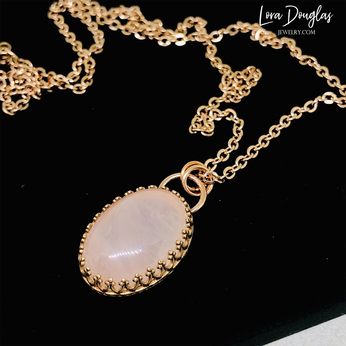 Close view of a natural rose quartz pendant showing the soft pink gemstone and bronze setting, paired with a stainless steel chain for a simple gemstone necklace traditionally associated with love.
