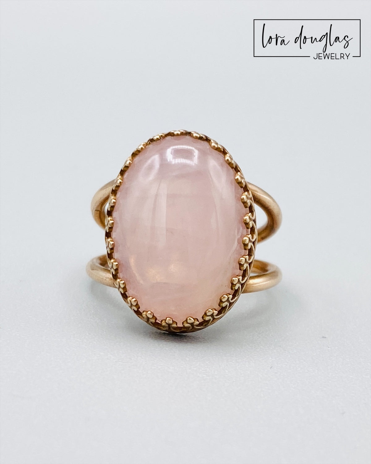 Close view of a natural rose quartz ring showing the soft pink color and character of the 18mm x 13mm gemstone in a warm bronze setting, a finished US size 6 ring and meaningful gift for her.
