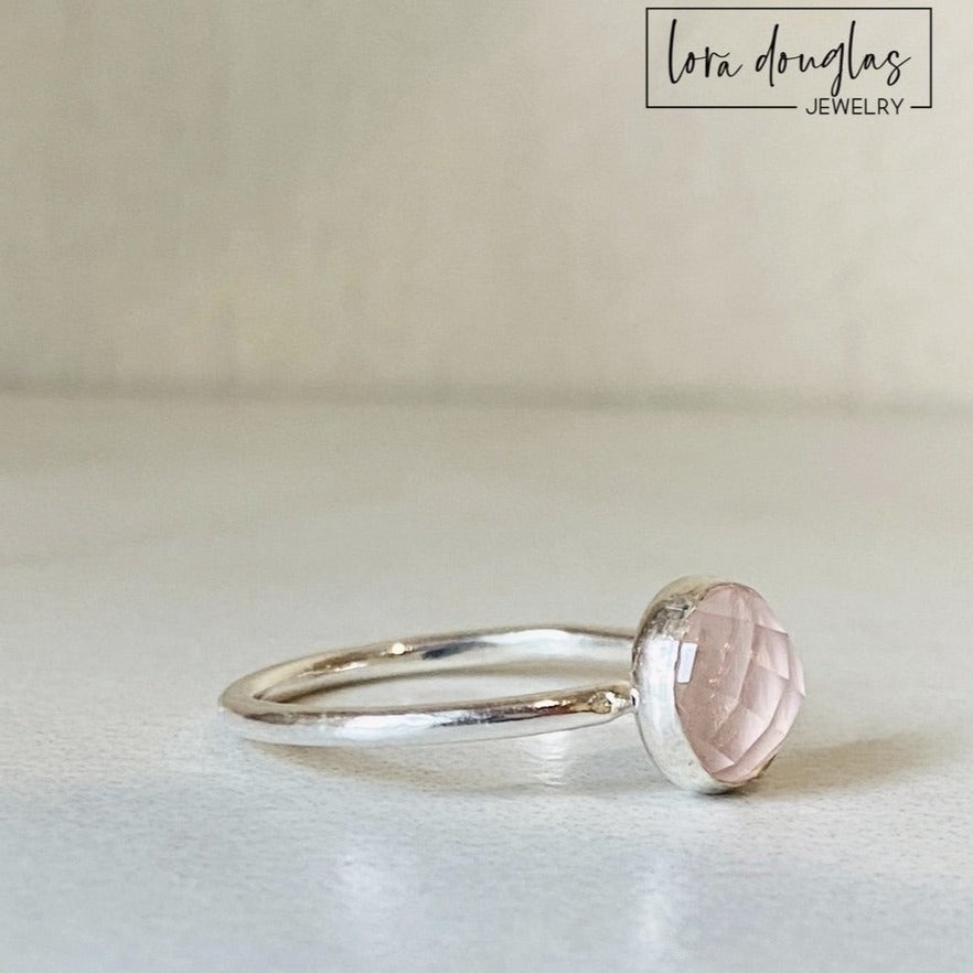 Close view of a natural rose quartz solitaire ring showing the faceted surface of the 8mm rose cut gemstone and sterling silver setting, a finished US size 7.5 ring for shoppers seeking pink gemstone jewelry.
