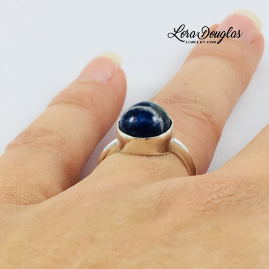 Close view of a natural sodalite ring showing the distinctive blue color and character of the 10mm gemstone in a 925 sterling silver setting, a finished US size 6 ring for natural stone jewelry lovers.
