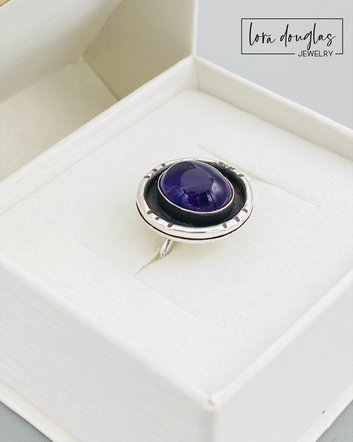 Close view of an amethyst shadow box ring showing the natural 12mm x 10mm purple gemstone framed by a handcrafted sterling and fine silver setting measuring approximately 17mm x 18mm.
